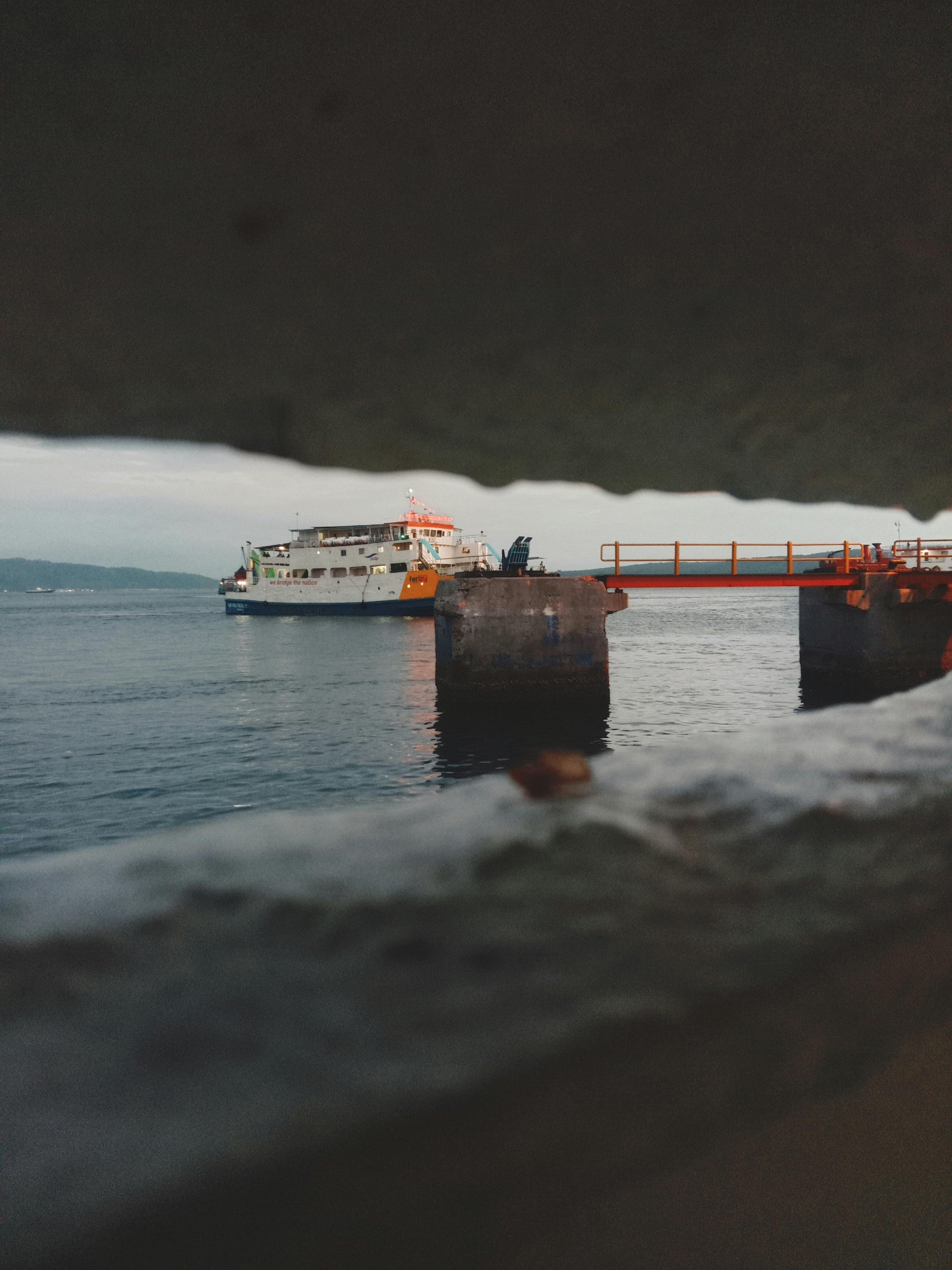 A ferry navigates past a dock as seen through a wall gap, highlighting industrial waterfront scenes.