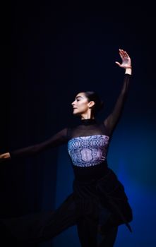 A graceful ballet dancer performs in a black dress against a blue background, showcasing elegance and poise.