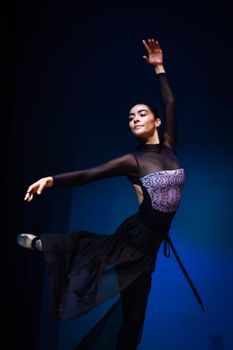Ballet dancer in a black dress striking a graceful pose against a blue background.