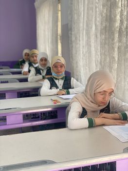 Middle Eastern teenage girls studying in a classroom, wearing hijabs and uniforms, focused and engaged.