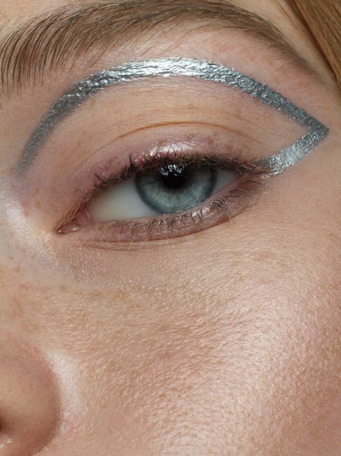 A detailed close-up of a woman's blue eye with unique silver eyeliner and natural makeup.