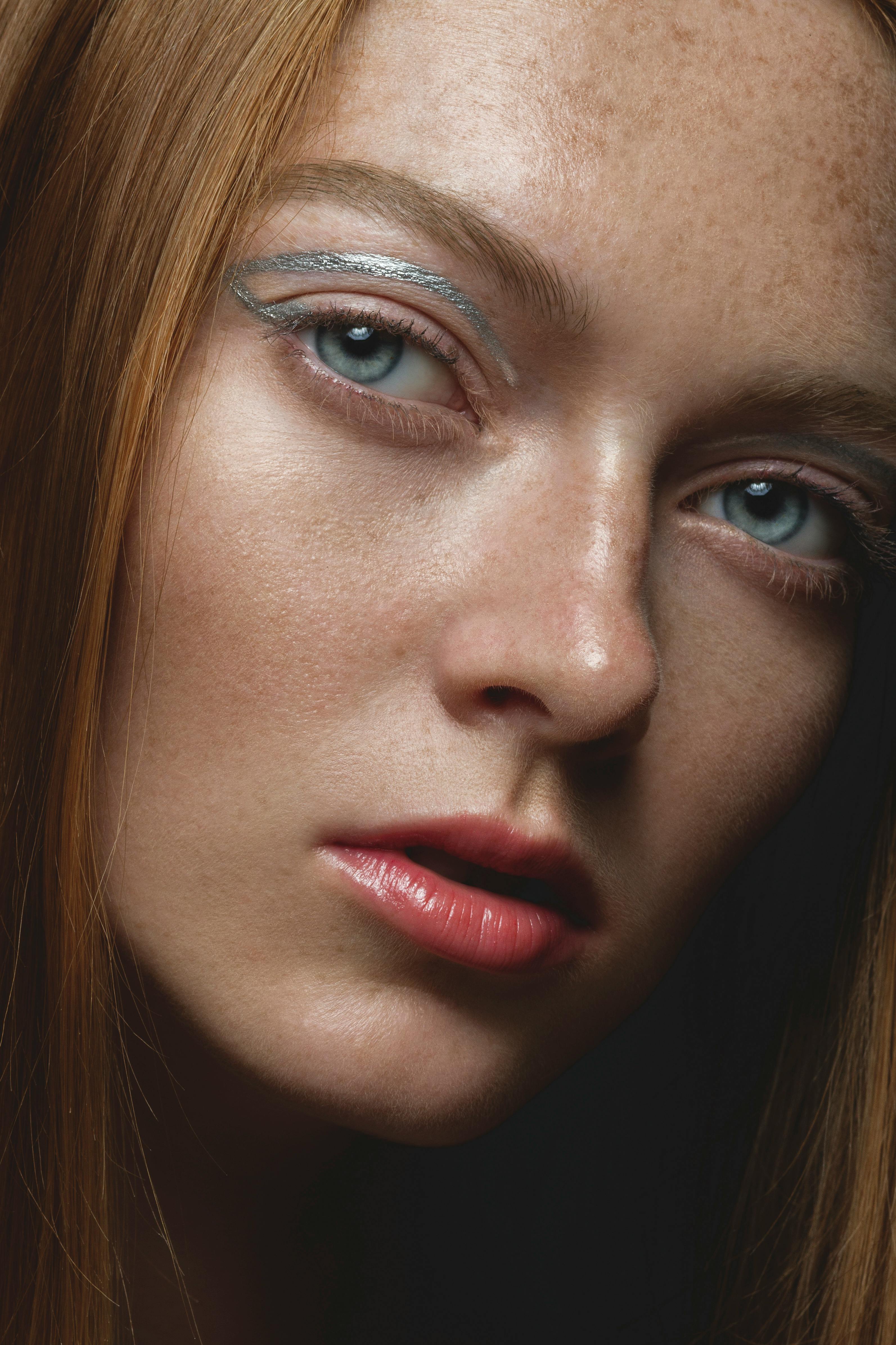Close-up portrait of a redheaded woman with distinctive freckles and elegant makeup.