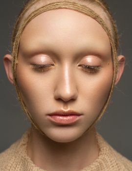 Close-up portrait of a woman with artistic makeup and rope headband in a studio setting.