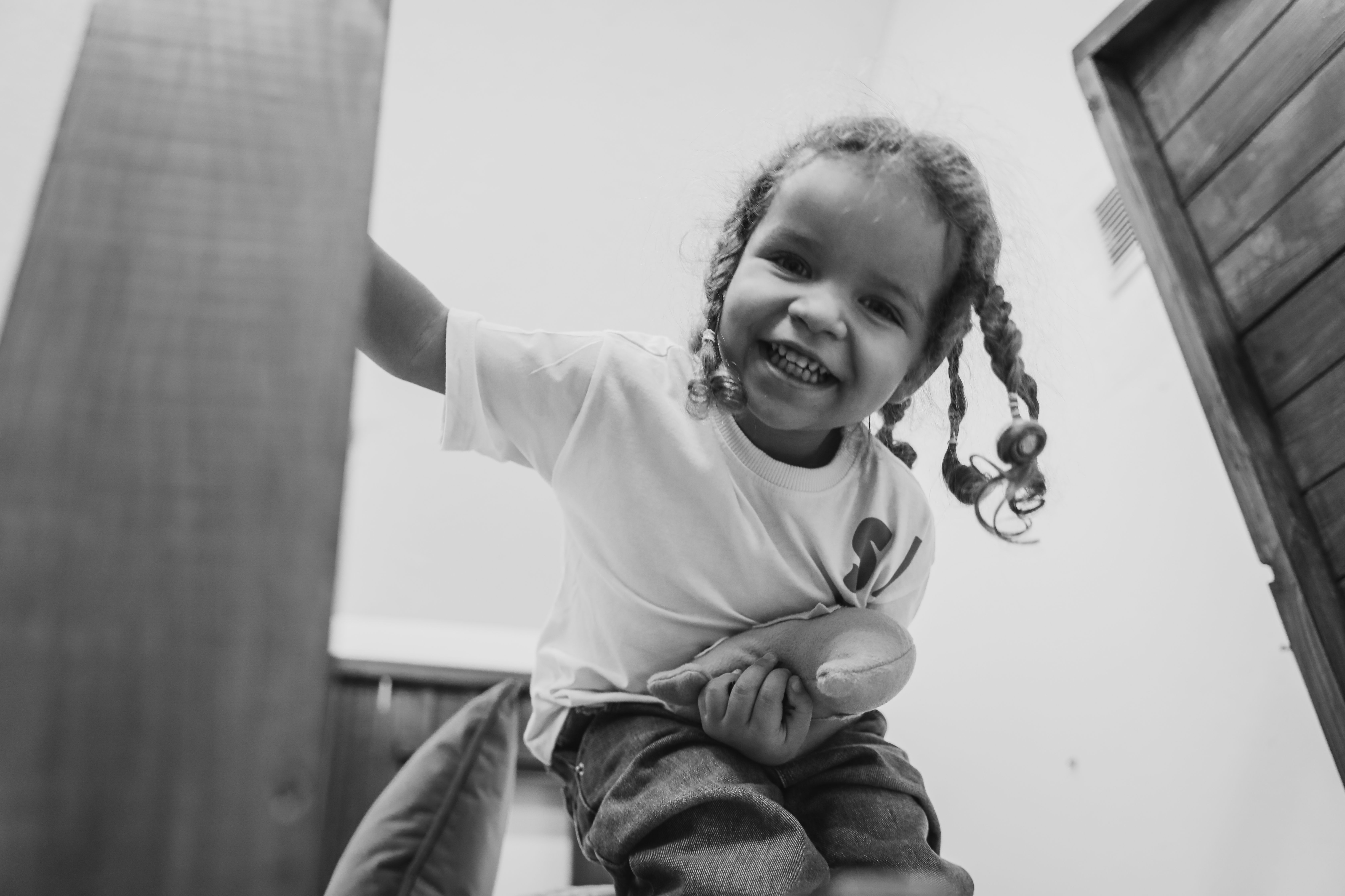 A smiling child with braided hair and a toy, expressing joy in a low angle shot.