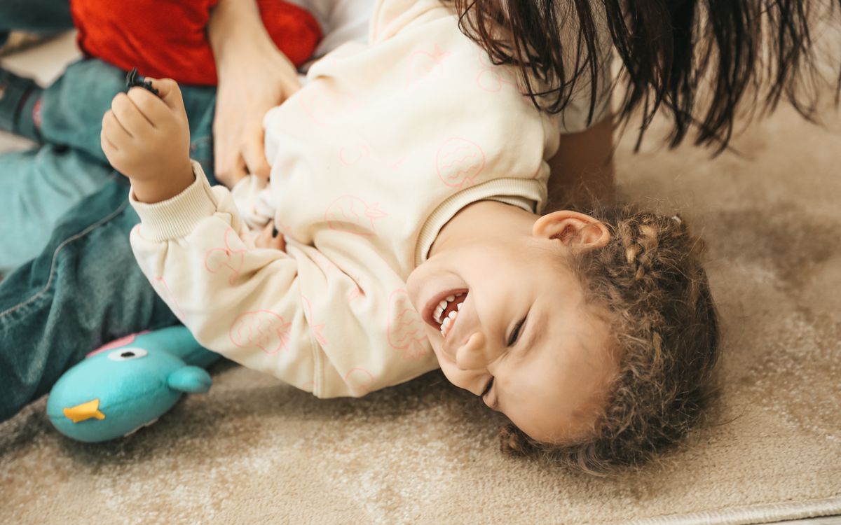A happy child laughs while playing with a parent indoors, capturing pure joy and innocence.