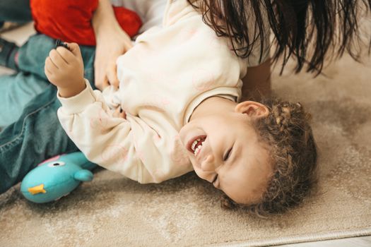 A happy child laughs while playing with a parent indoors, capturing pure joy and innocence.
