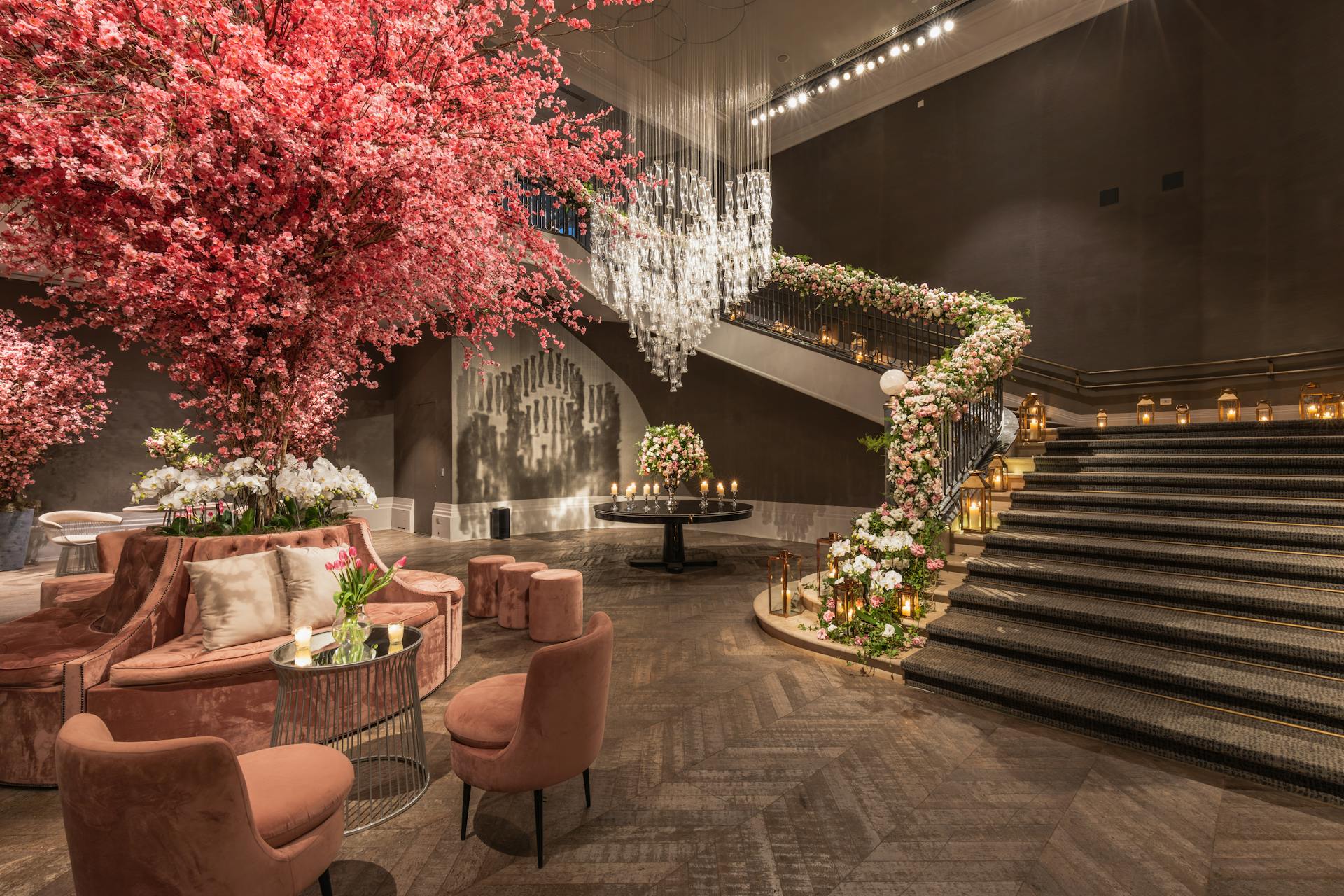 Stunning hotel lobby adorned with pink floral arrangements and elegant seating area under a grand staircase.