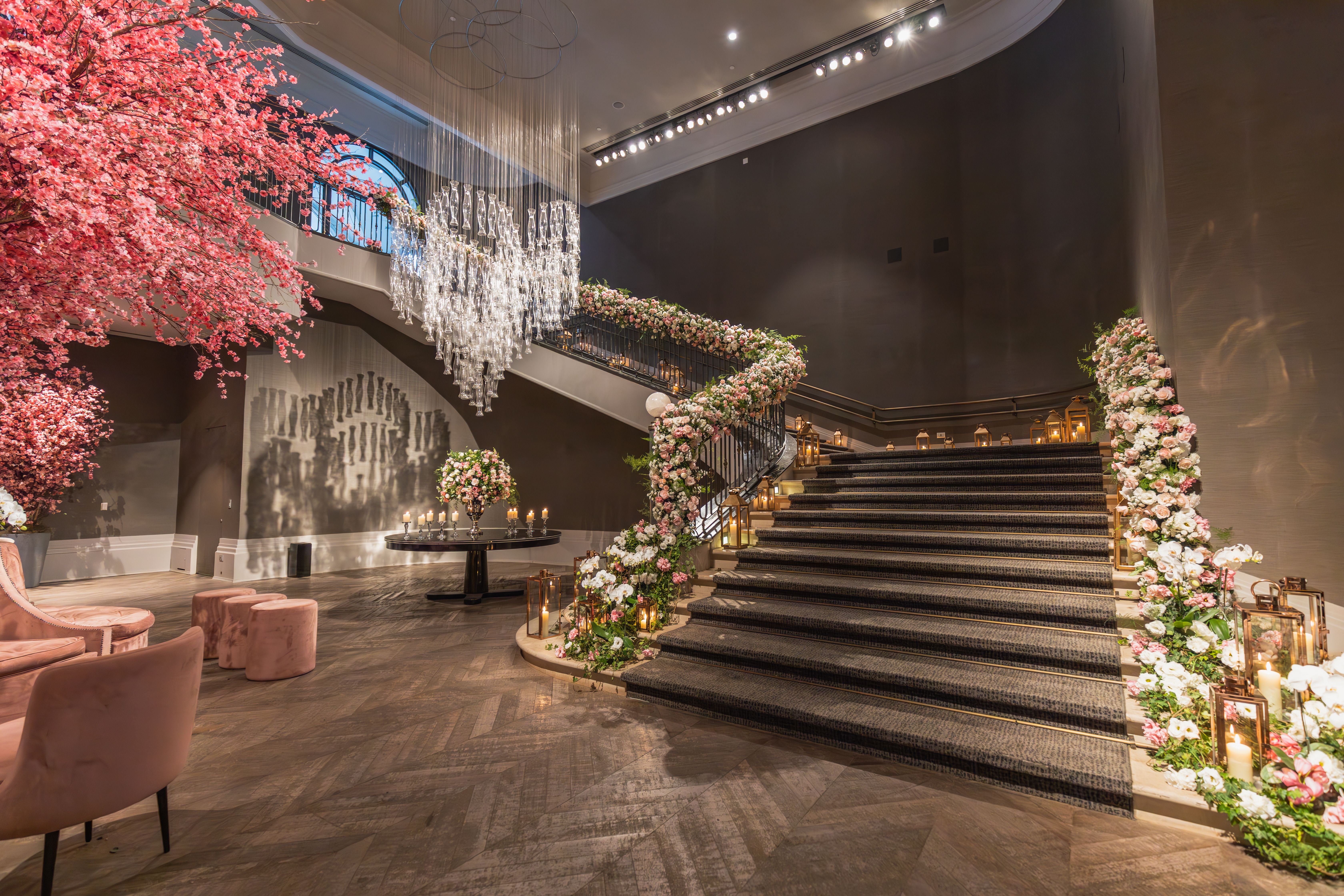 An opulent indoor staircase beautifully decorated with flowers, chandelier, and ambient lighting.
