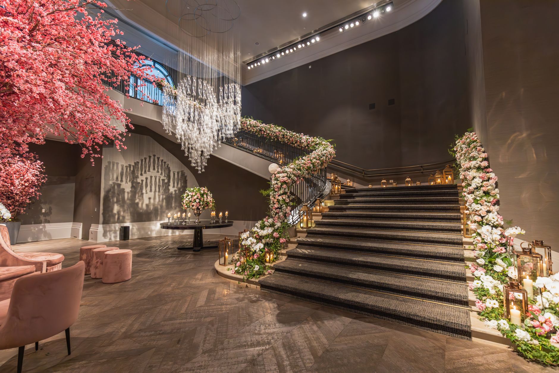 An opulent indoor staircase beautifully decorated with flowers, chandelier, and ambient lighting.