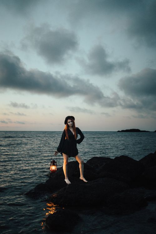 Free Woman holding a lantern on rocky seashore at twilight, Türkiye's coast. Stock Photo