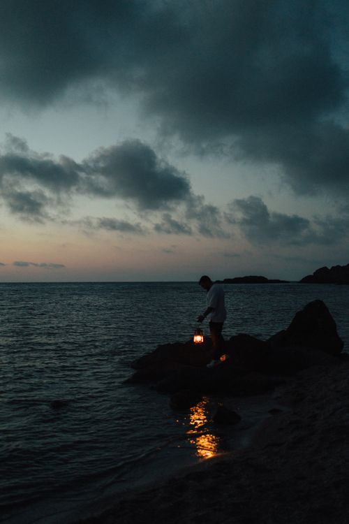 Free Silhouette of a person holding a lantern by the sea at dusk, creating a serene evening scene. Stock Photo