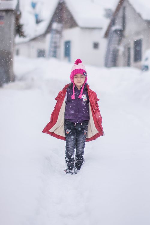 Free Young girl in warm clothing walking through a snow-covered village street during winter. Stock Photo