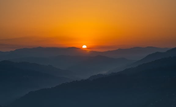 A stunning view of the sun setting over rolling hills and mountains, creating a warm and dramatic sky.