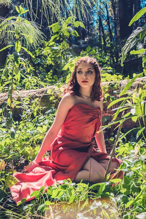 Woman in Red Dress Sitting on Ground in Forest