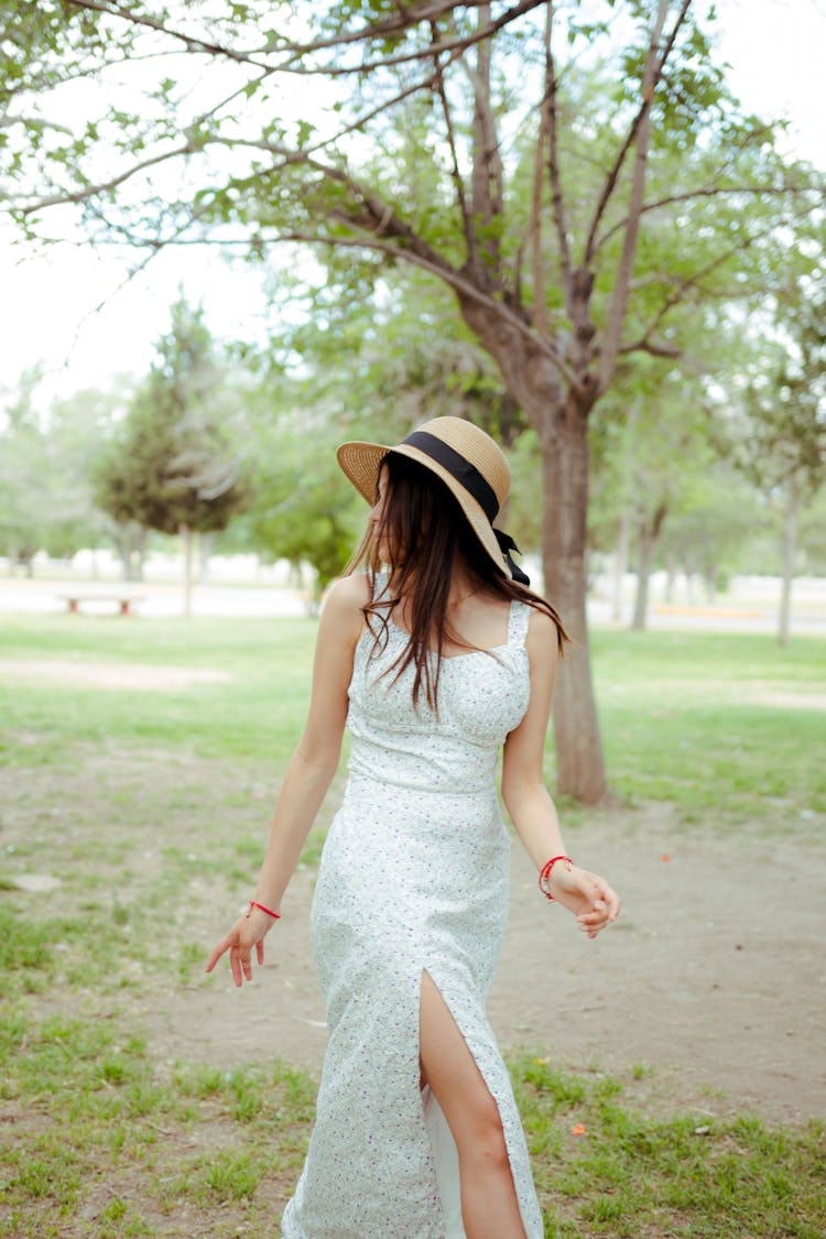 Young Woman In A Dress And Hat Walking In The Park