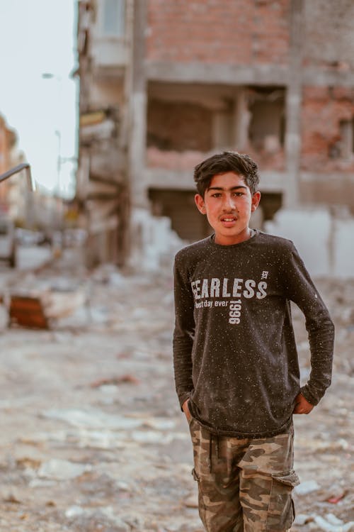 A Boy Standing in the Ruins of Buildings in City 