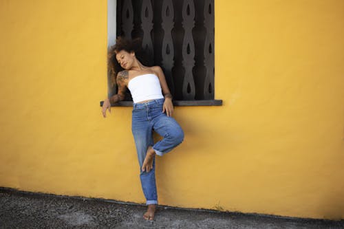 Young Woman in a White Tube Top and Jeans Posing by the Window