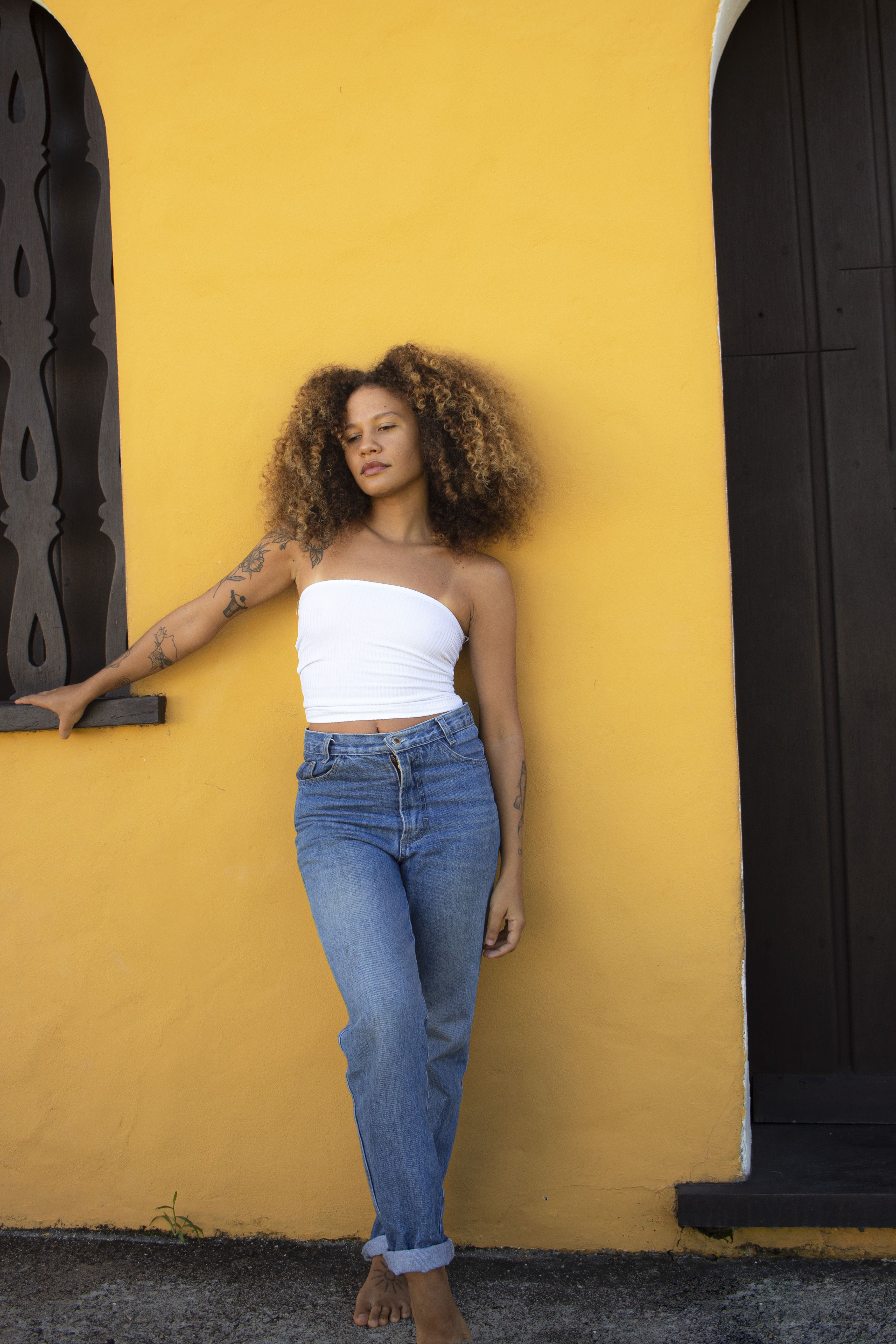 Stylish woman with curly hair poses against a yellow wall in Porto Seguro, Brazil.
