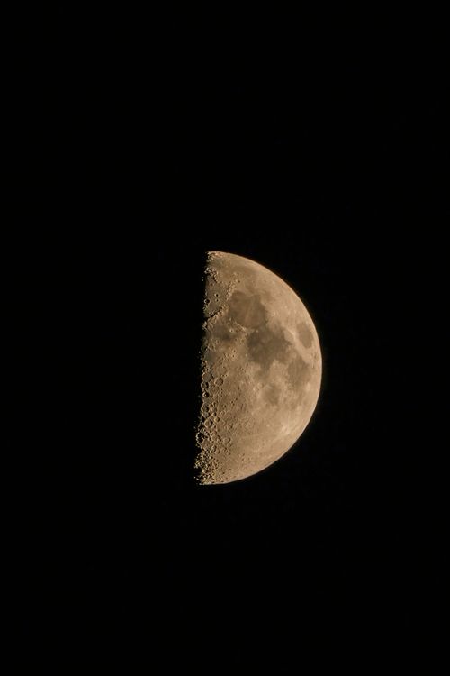 Free A detailed view of the half moon glowing in the dark night sky, showcasing lunar textures. Stock Photo