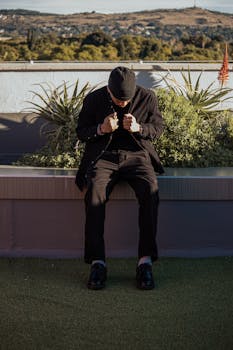 Stylish man in black sitting on rooftop garden in urban setting.