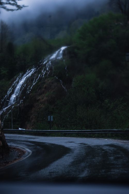 Free A scenic view of a winding road through foggy mountains with a cascading waterfall. Stock Photo