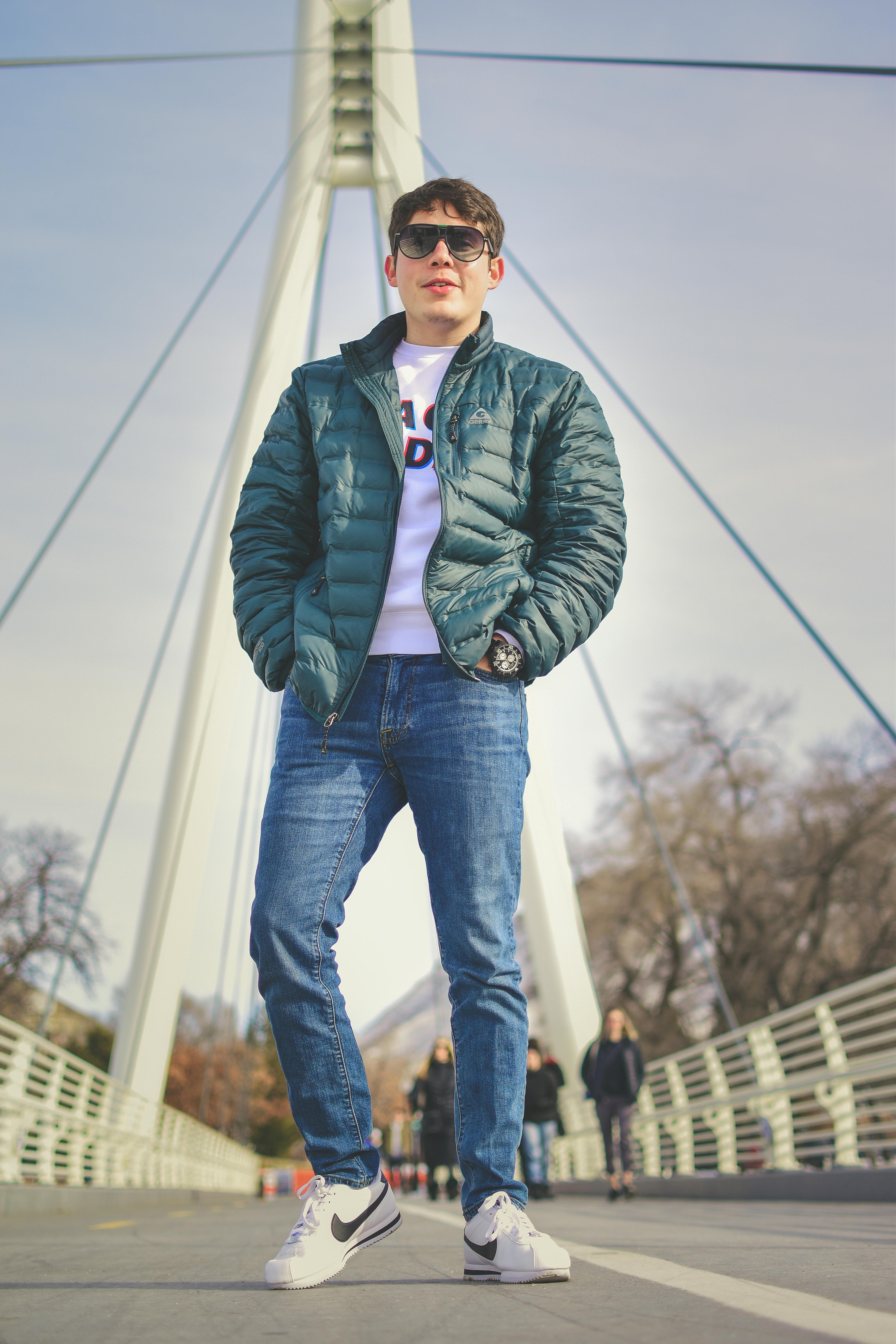 在现代城市桥梁上，时尚的年轻人穿着绿色夹克和牛仔裤，展示冬季时尚