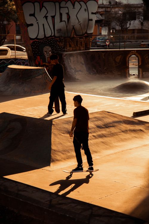 Free Two teenagers skateboarding at an urban skate park during sunset, casting long shadows. Stock Photo