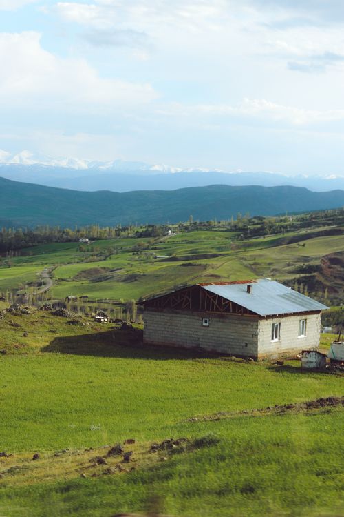 Free A house in a tranquil rural landscape with lush greenery and distant mountains. Stock Photo