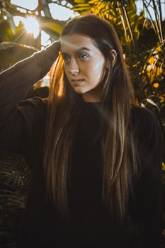 A woman in a black shirt poses outdoors with sunrays highlighting her face and long hair.
