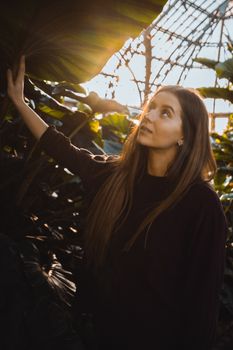 Elegant woman in a sunlit greenhouse surrounded by vibrant foliage, embracing nature.
