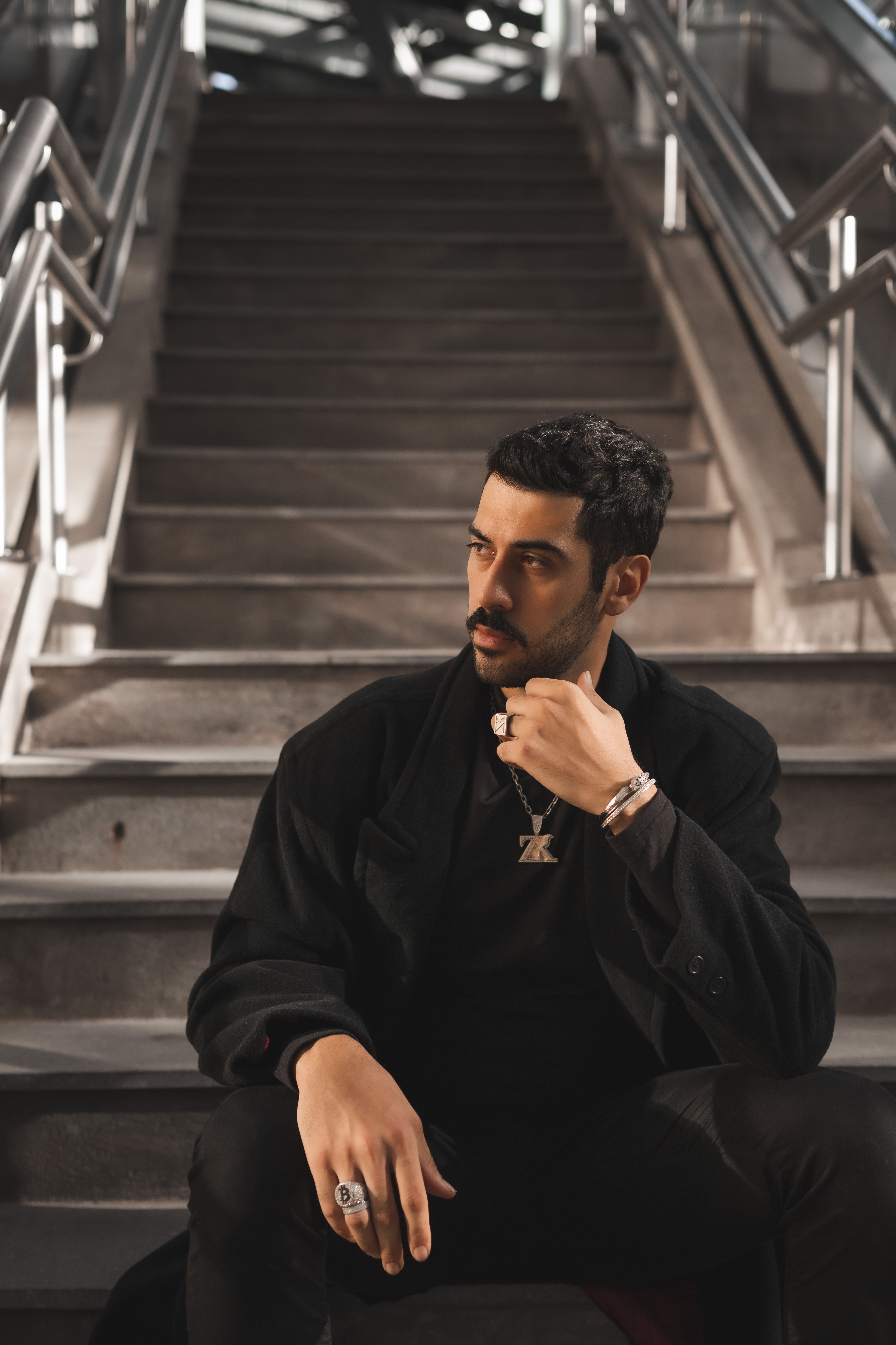 A stylish man poses confidently on modern indoor stairs, showcasing fashion sense.