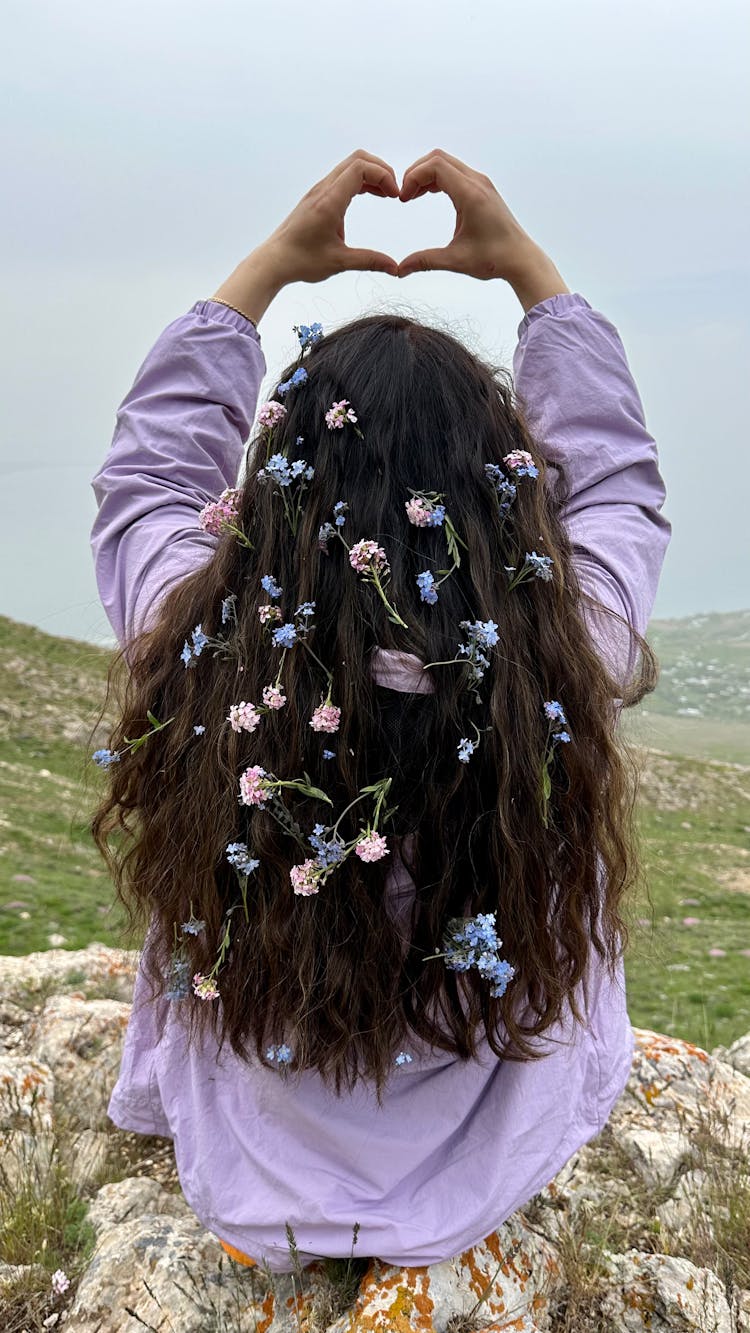 Woman With Flowers In Her Hair Sitting On Rock Rising Up Hands Forming Heart Shape