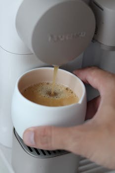 Hand pouring fresh coffee into a mug from a coffee machine indoors.