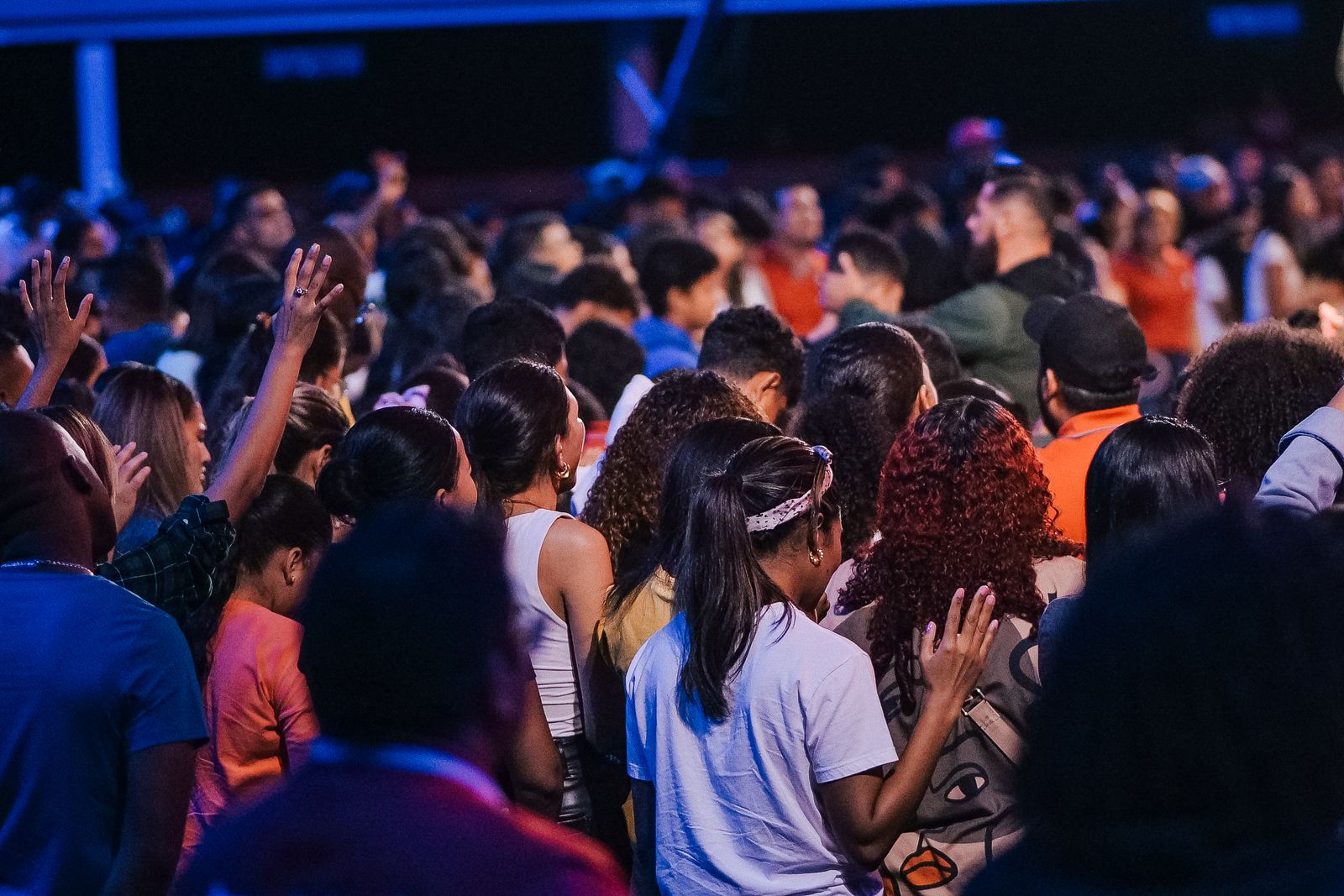 A large congregation standing together in worship, raising hands in unity.