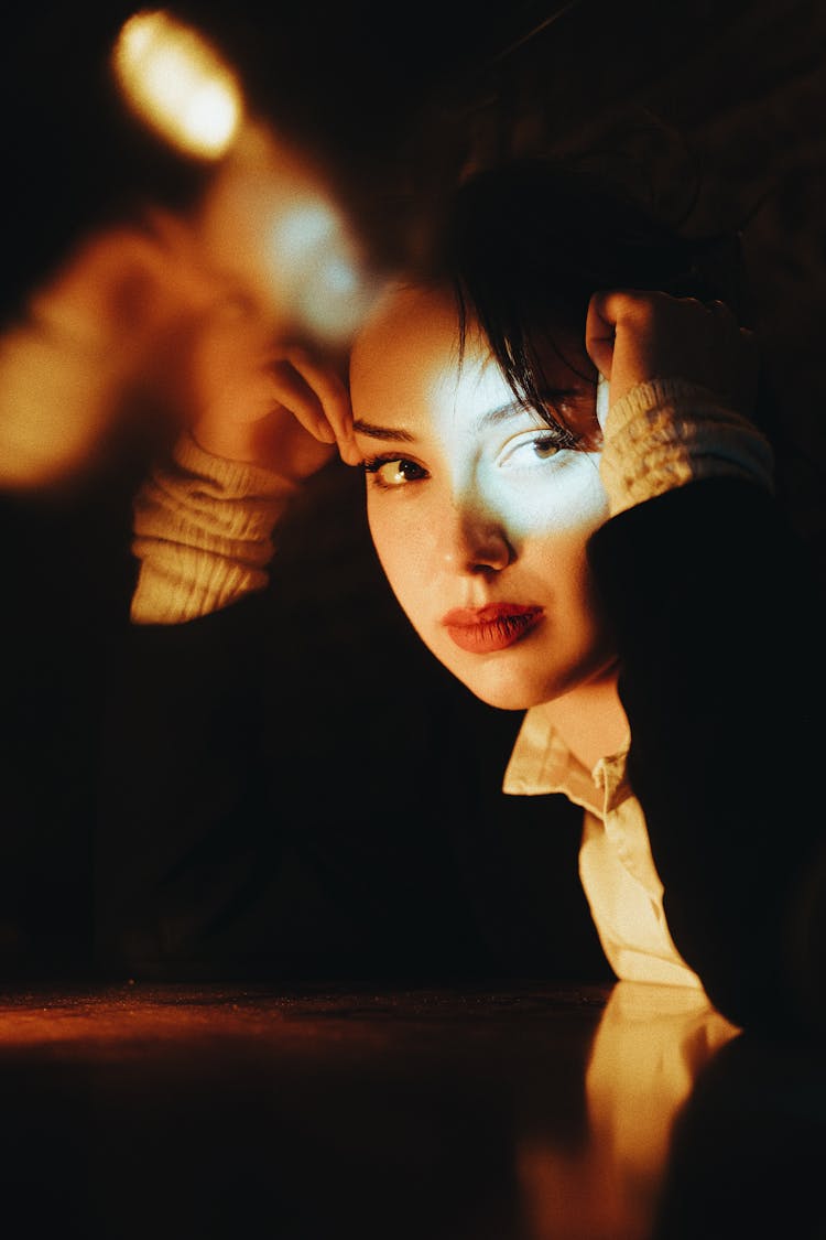 Young Woman Sitting At The Table In A Dark Room 