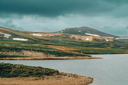 Scenic View of a Lake and Hills and Fields under an Overcast Sky 