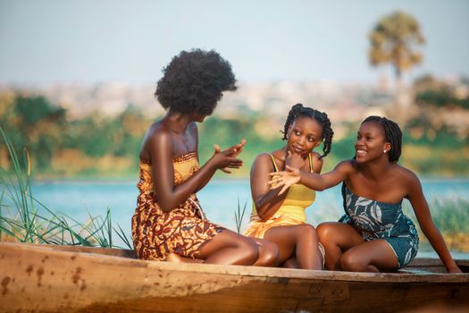 Three women enjoy a sunny day in Accra, Ghana, laughing and relaxing in a canoe on a river.