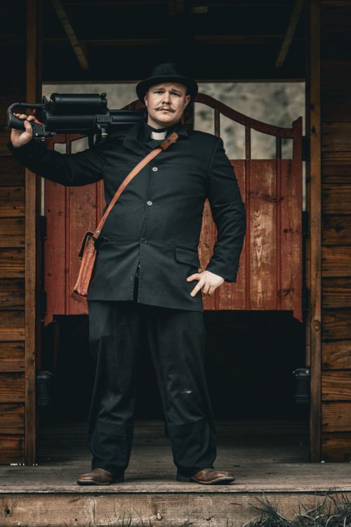 Free A man dressed in historical attire stands confidently with a machine gun at a saloon entrance. Stock Photo