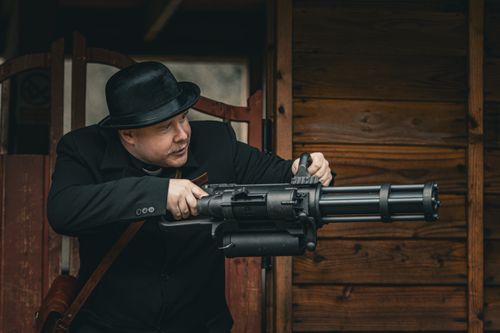 Free Man dressed in retro attire holding a minigun, posing for a historical reenactment. Stock Photo