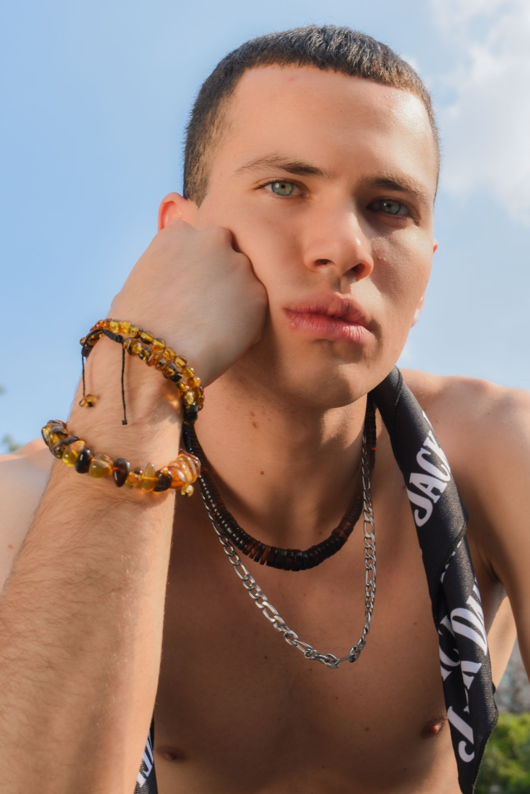 Portrait of a young man wearing fashionable bracelets and necklaces outdoors in daylight.