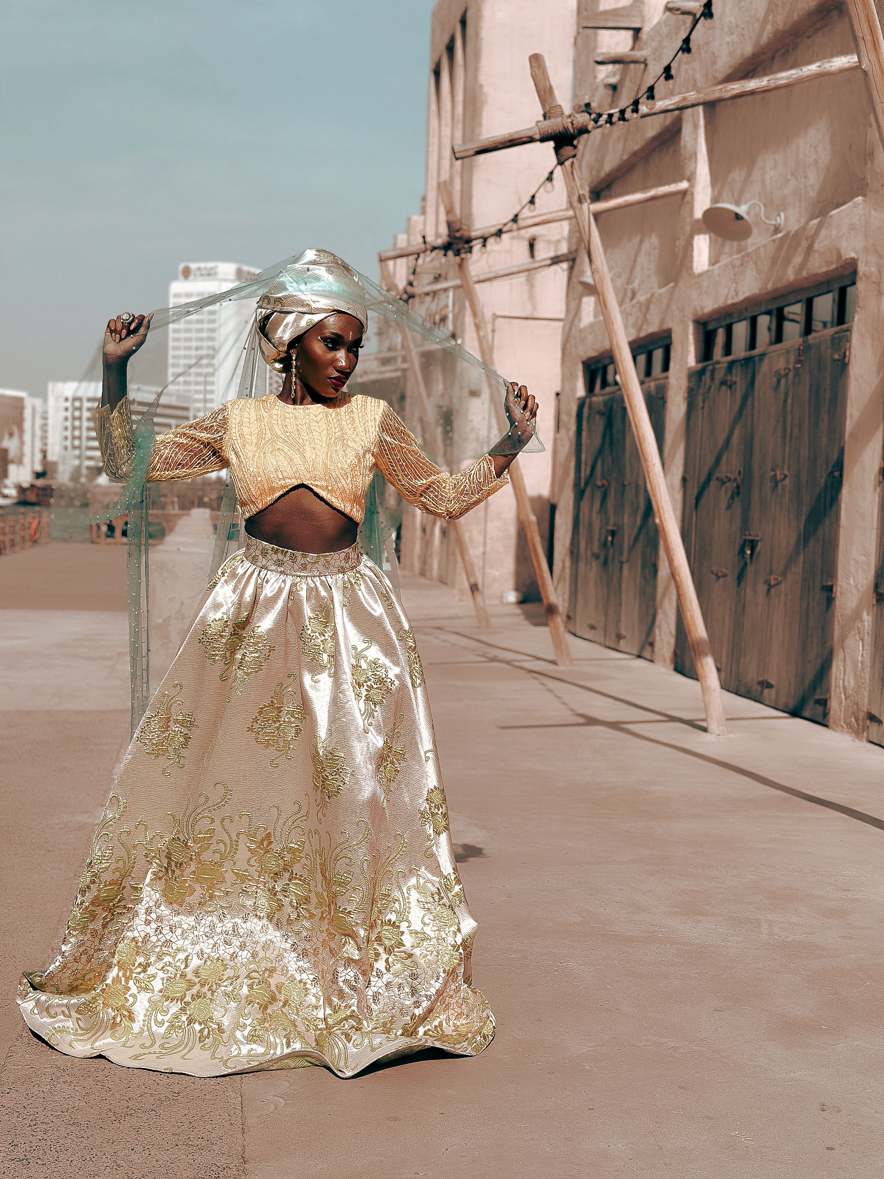 A stylish African woman poses outdoors in elegant attire with a city backdrop.