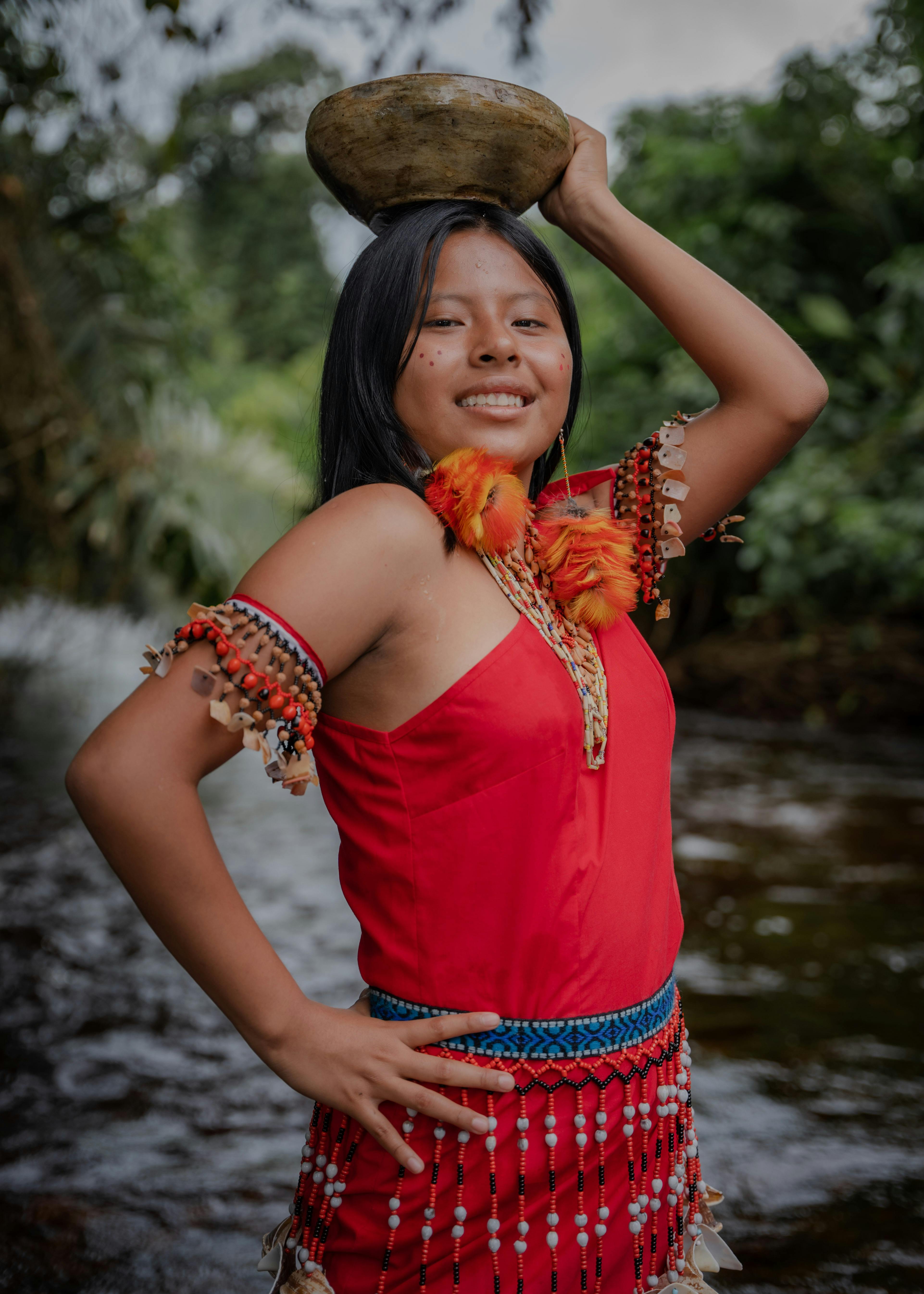 Smiling woman in traditional clothing poses with a bowl by a river in Peru.
