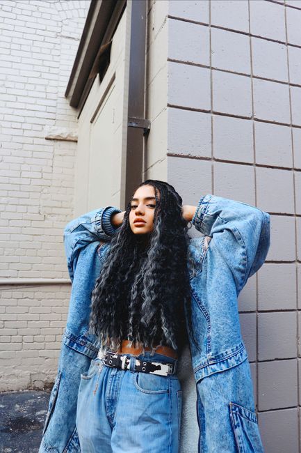 Stylish young woman posing in denim outfit against urban backdrop. Fashion statement in modern setting.