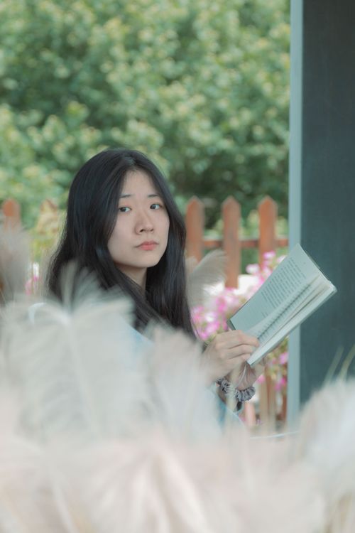 Free A young woman with dark hair holds a book outdoors, surrounded by greenery and pampas grass. Stock Photo