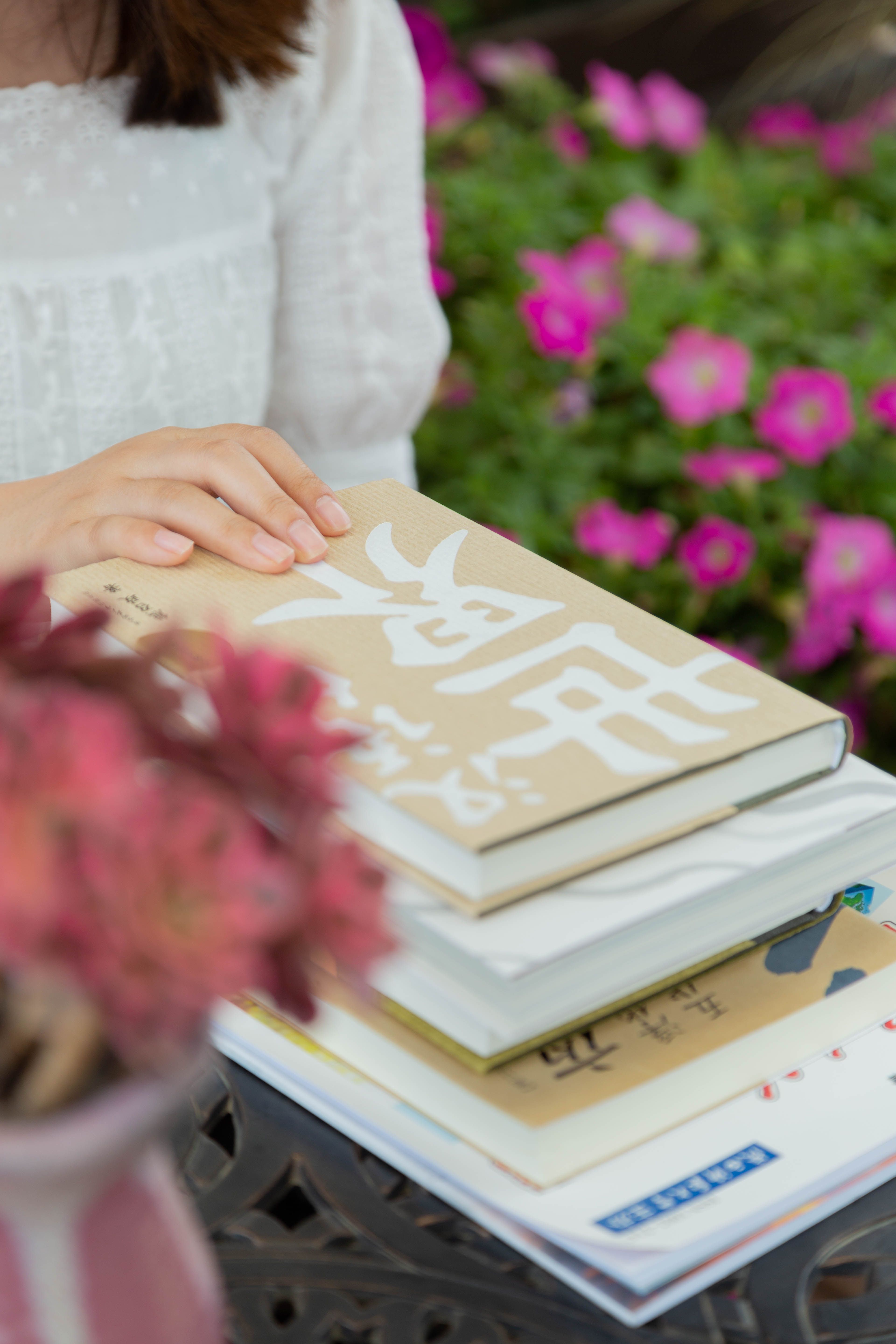 A woman enjoys relaxing with books in a scenic garden full of blooming flowers.