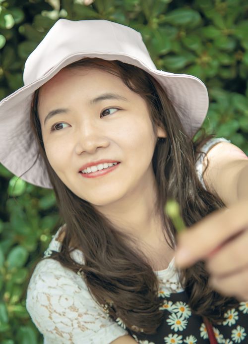 Free Smiling young woman in a hat surrounded by greenery, enjoying summer. Stock Photo