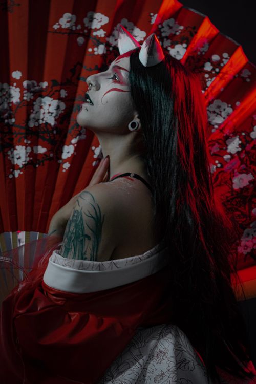 Free Captivating portrait of a woman in a red costume with tattoos, holding a fan. Stock Photo