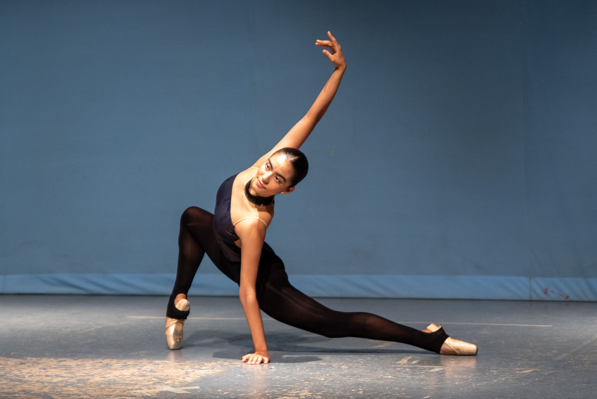 Bailarina en un estiramiento profundo sobre el suelo, con un brazo extendido hacia arriba