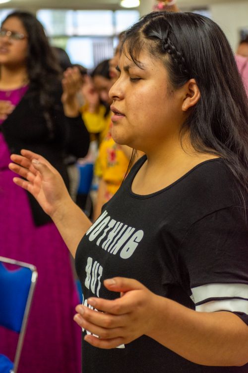 Free A woman standing with eyes closed, participating in a group prayer indoors. Stock Photo
