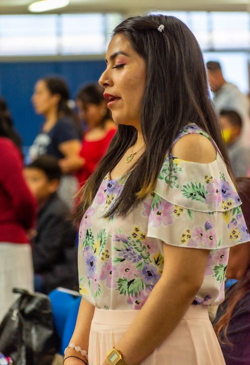 Free Young woman with long hair and floral dress standing in an indoor gathering, eyes closed. Stock Photo